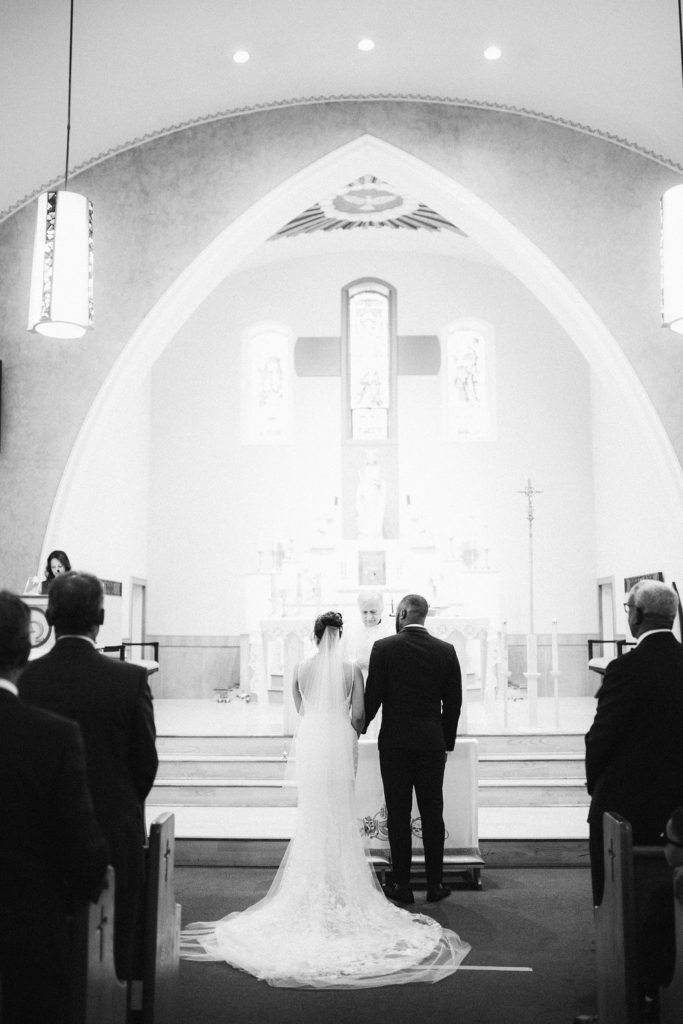 Bride and groom stand in front of priest holding hands