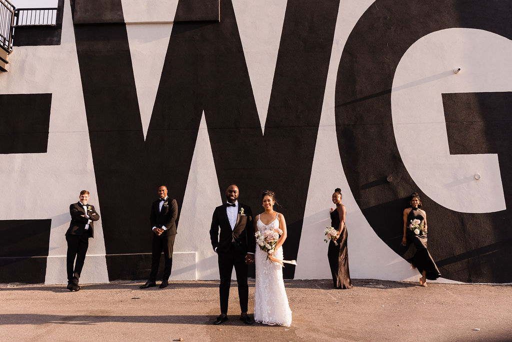 Wedding party posing with EWG graphic on the exterior wall at Eglinton West Gallery wedding